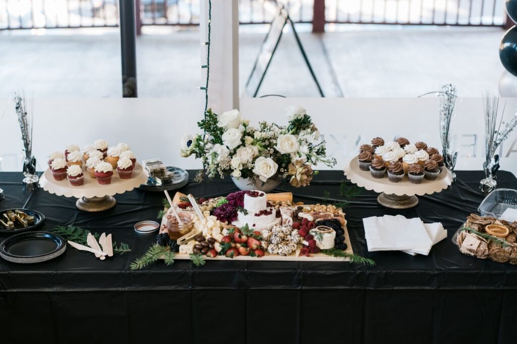 An elegantly arranged dessert table featuring cupcakes, a cheese platter, and floral decor, perfect for events.