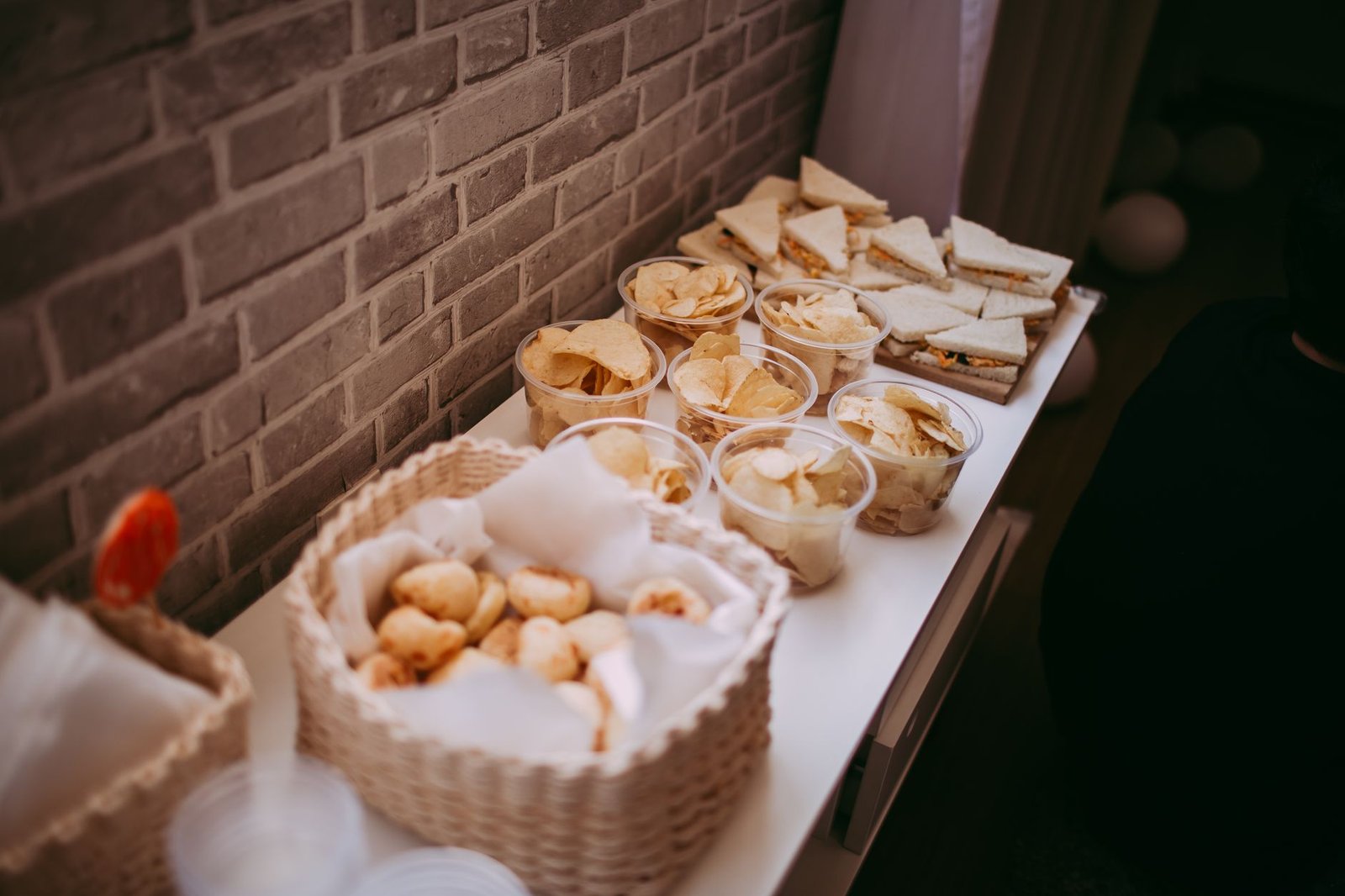 A variety of snacks and sandwiches on a buffet table against a brick wall.