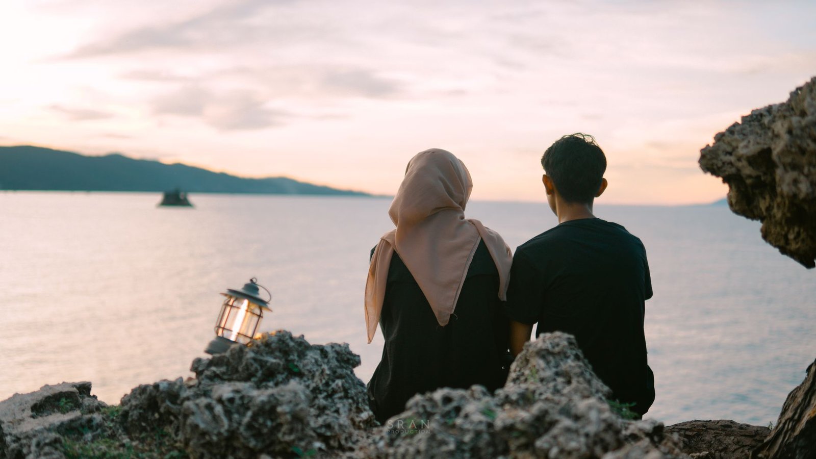 Pemandangan matahari terbenam yang tenang dengan sepasang kekasih yang duduk di bebatuan di tepi laut di Aceh, Indonesia.