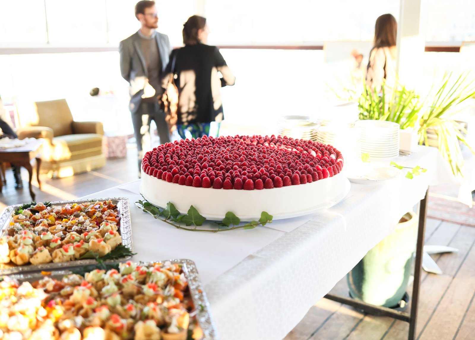 Elegant buffet setup with a raspberry cake centerpiece at an indoor event.