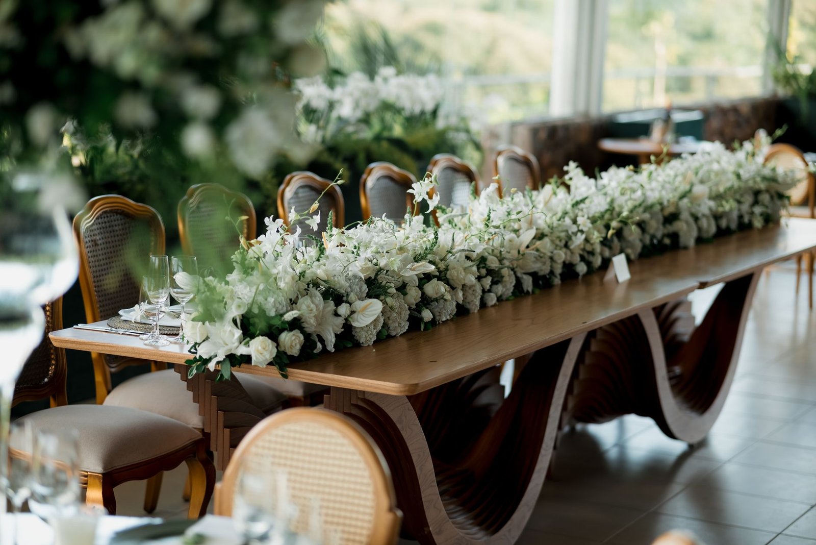 Long wooden table with lavish white floral centerpiece, perfect for weddings.