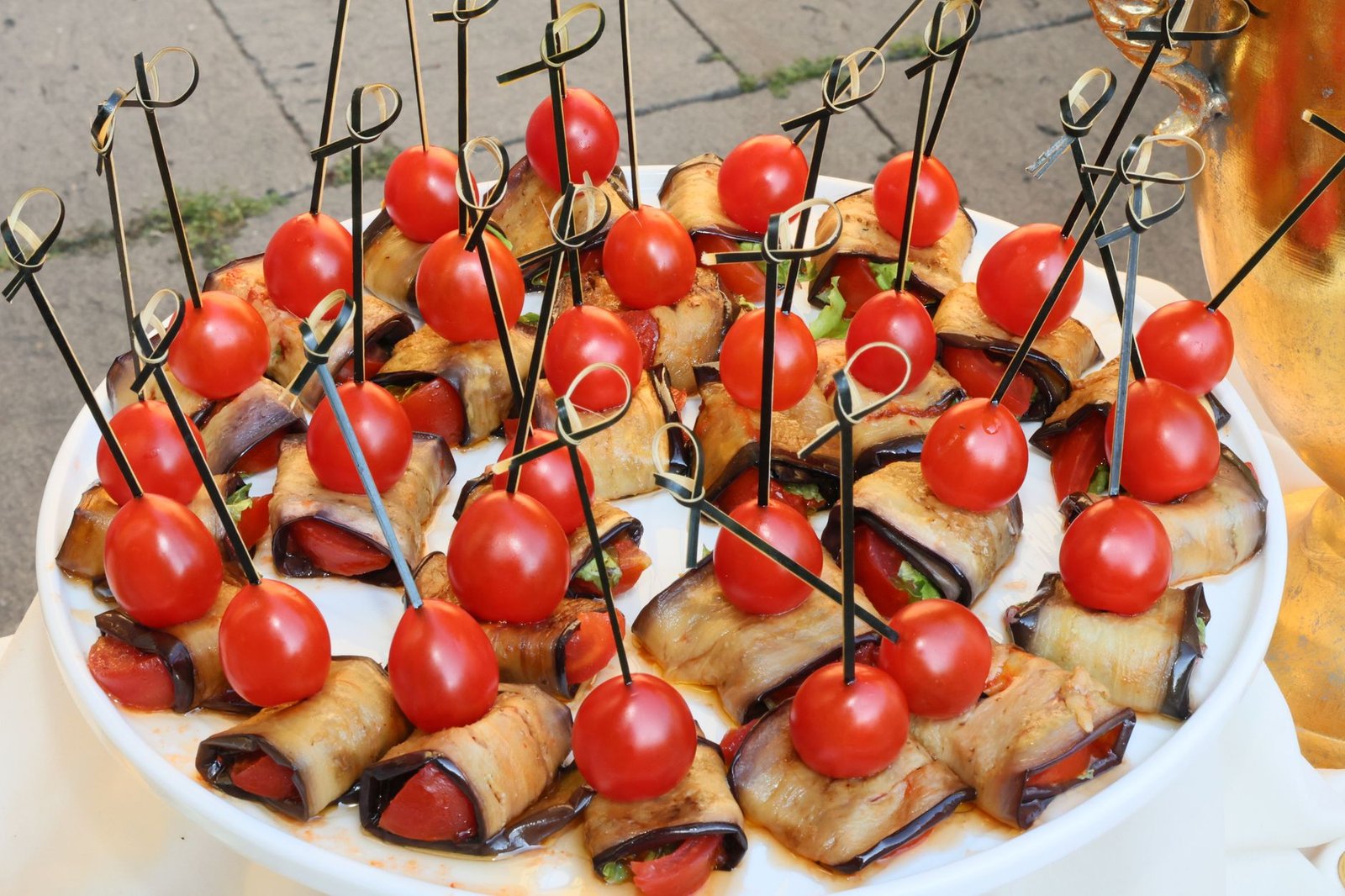Appetizing platter of grilled eggplant rolls with cherry tomatoes on skewers, perfect for party snacks.