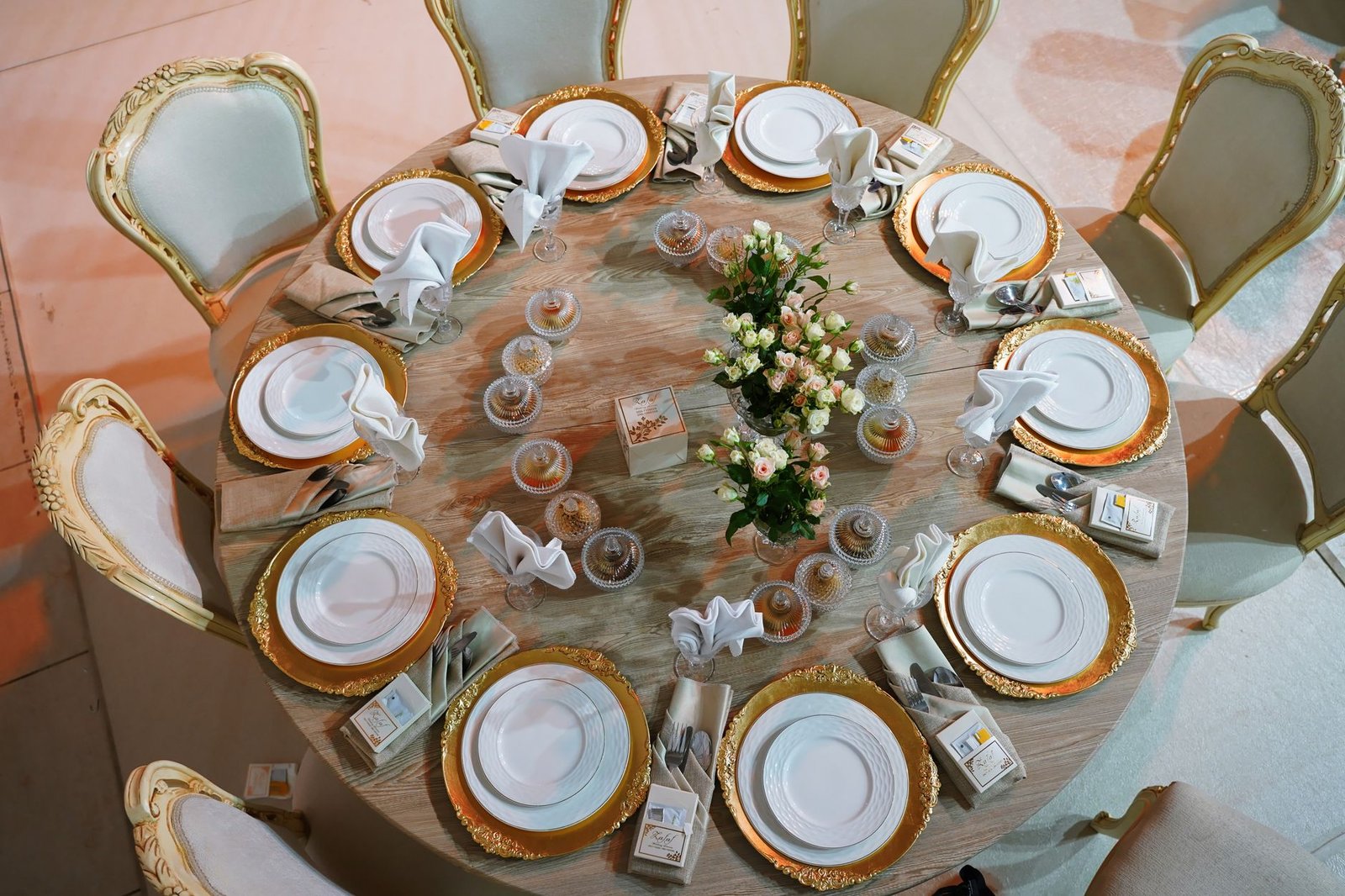Luxurious round table with golden plates and roses, meticulously set for a wedding celebration.