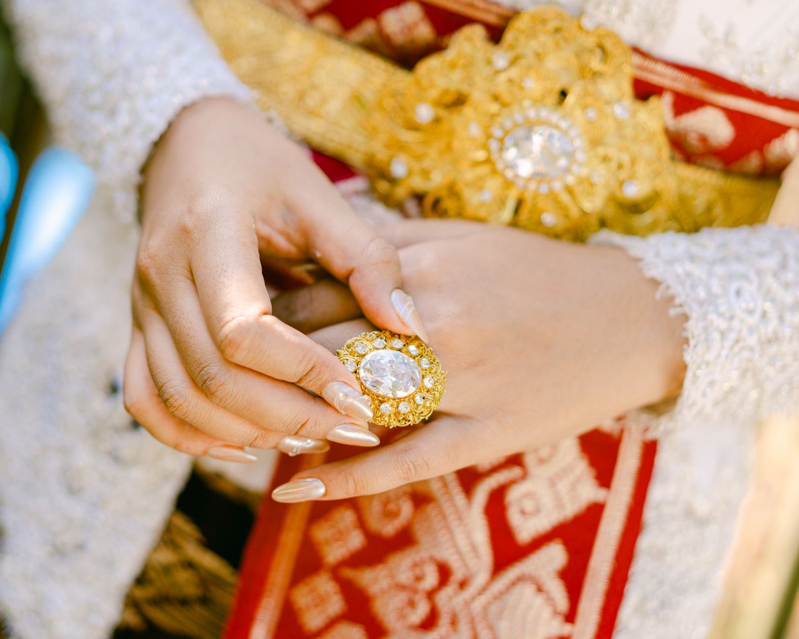 Tampilan jarak dekat tangan dalam pakaian tradisional berhias memegang cincin emas yang rumit, memperlihatkan keanggunan budaya.