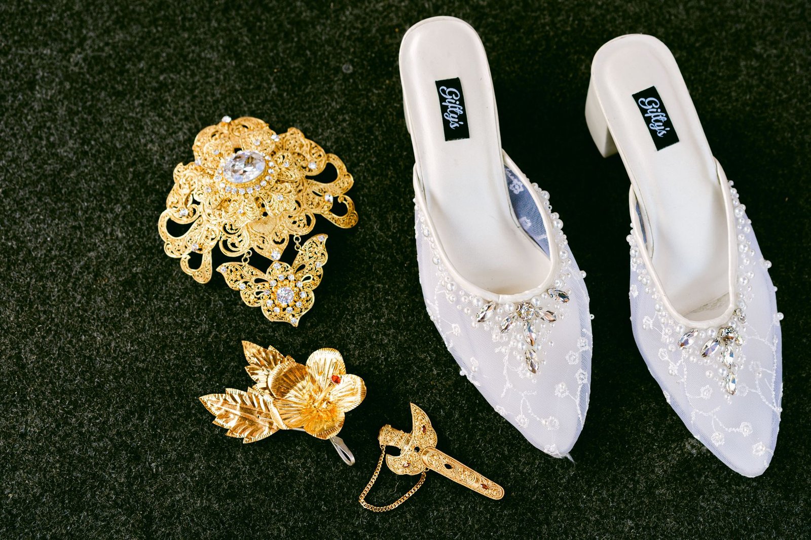 Sepatu pengantin putih yang cantik dihiasi dengan aksesoris permata emas pada latar belakang hitam.