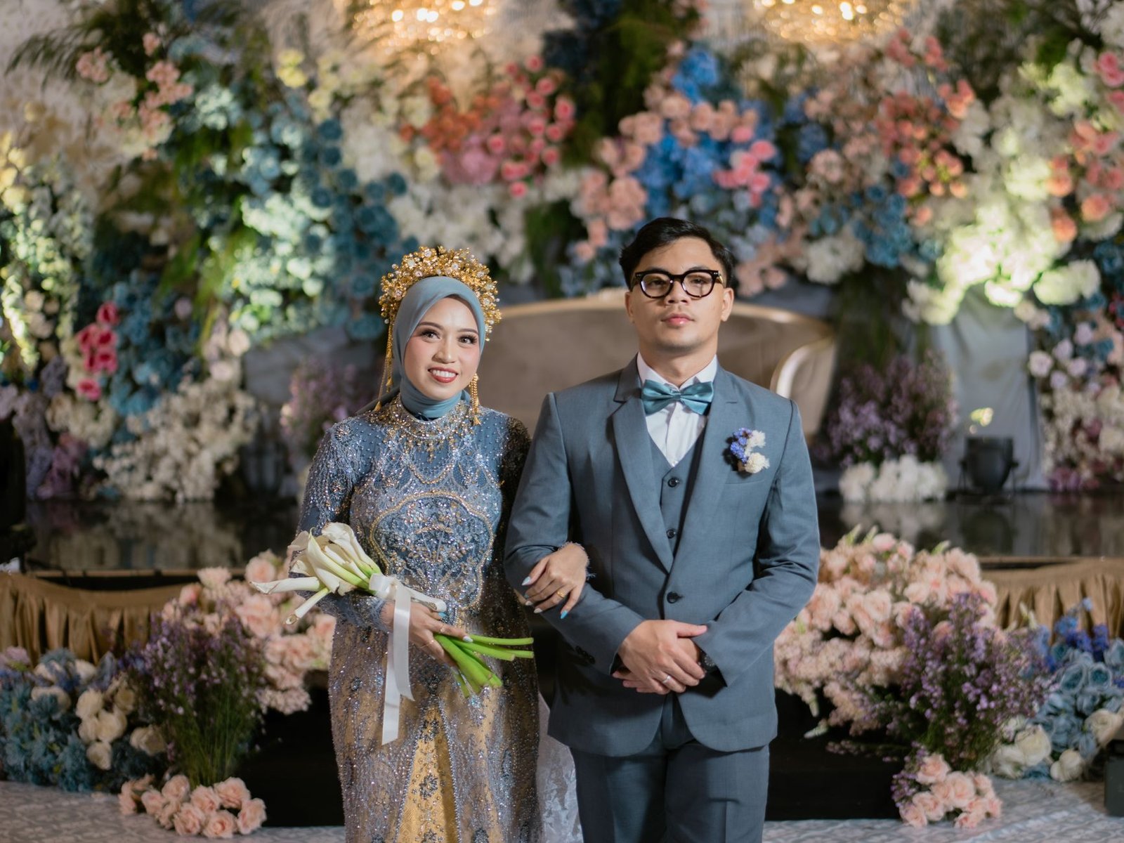 Pasangan Indonesia yang cantik merayakan pernikahan mereka di Kendari, dikelilingi oleh latar belakang bunga-bunga.