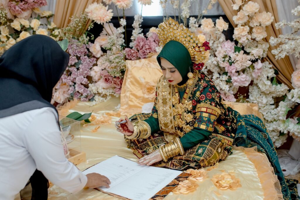 Seorang mempelai wanita menandatangani akad nikah dalam suasana pernikahan Indonesia yang meriah.