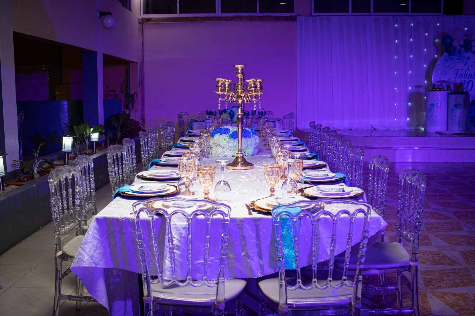 Luxurious formal table setting with clear chairs and centerpiece in a warmly lit room.