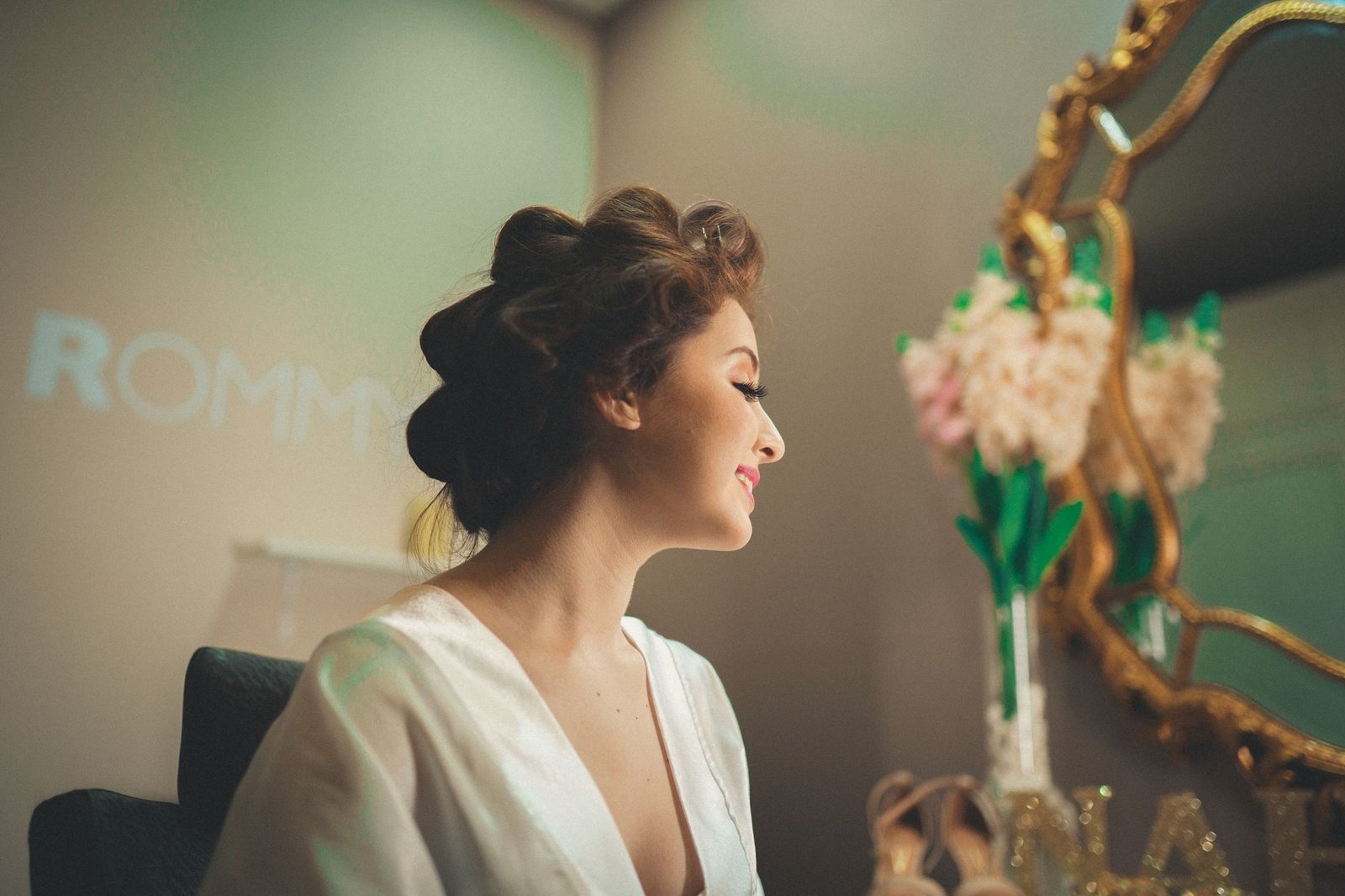 Elegant woman with hairstyle in front of vintage mirror, indoors, smiling.