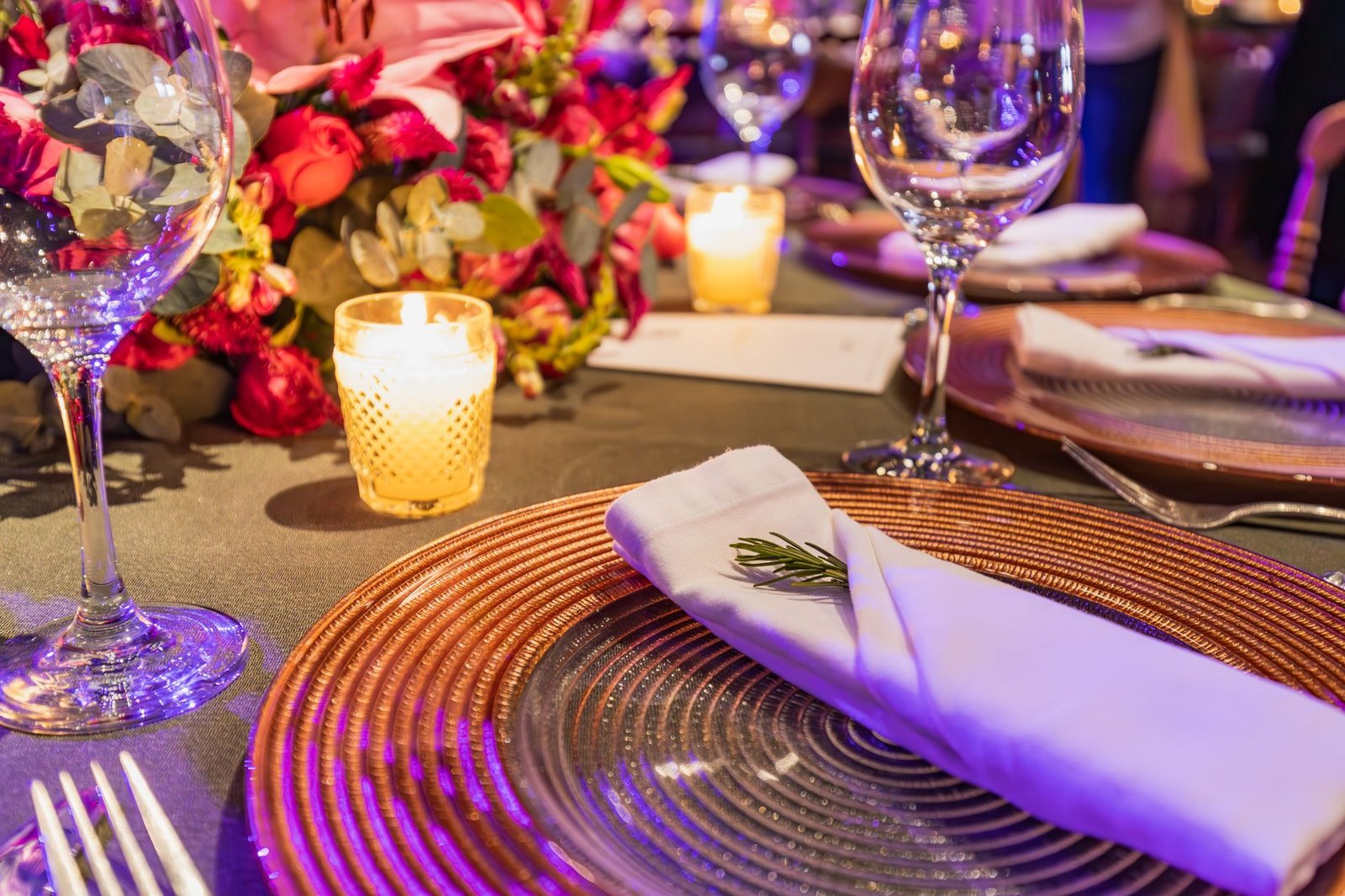 Close-up of a chic table setting with flowers, glassware, and candlelight ambiance.