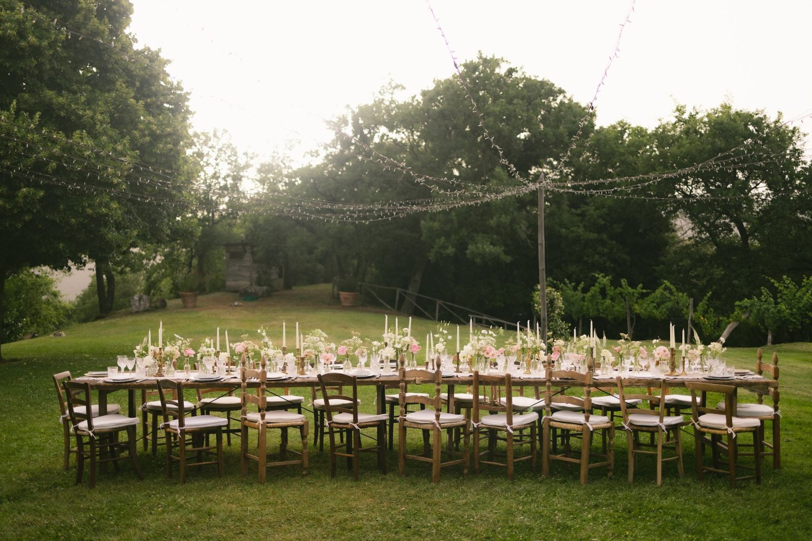 Beautiful outdoor wedding reception table setup with floral decorations and string lights in a garden.