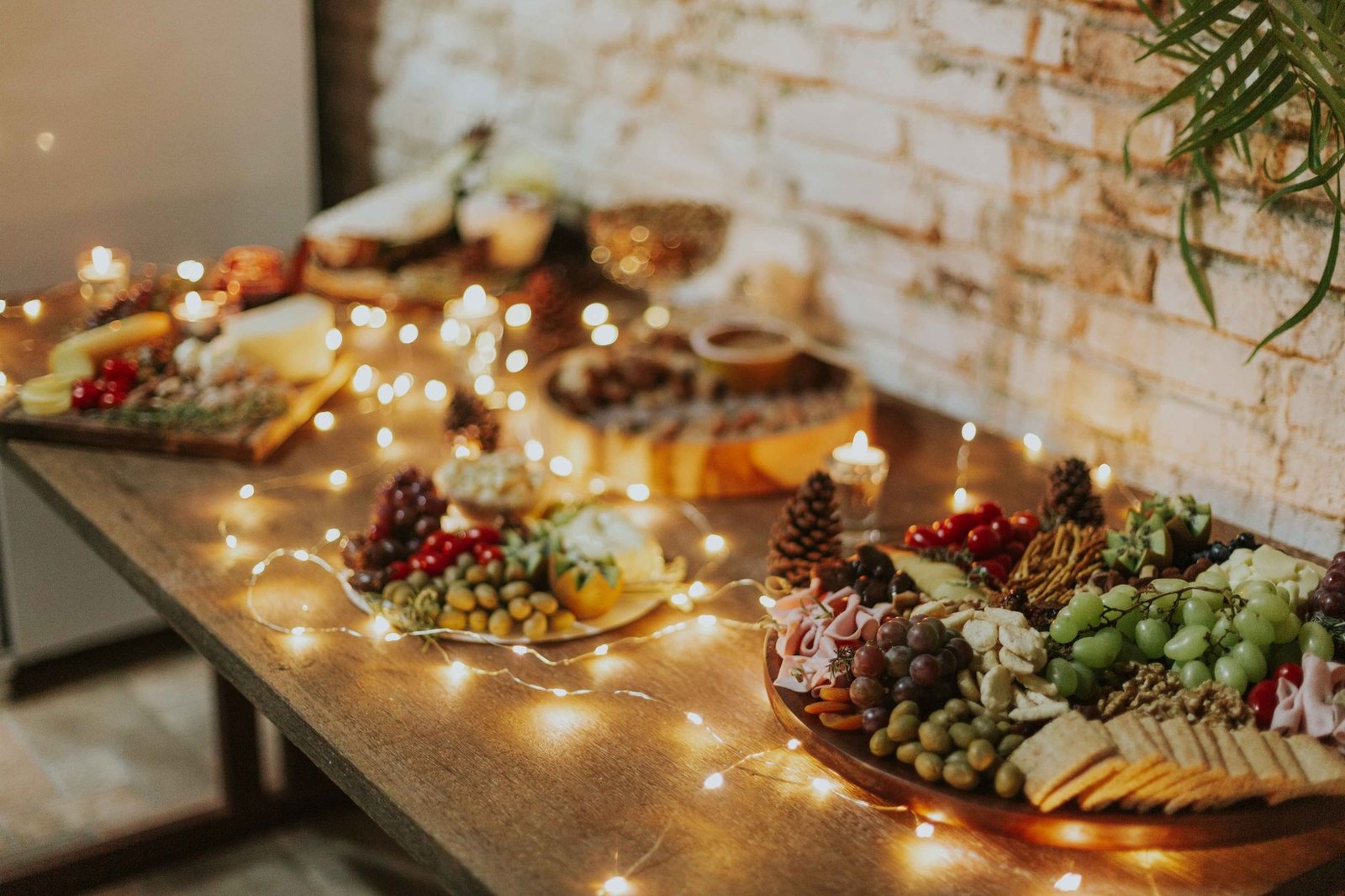 Cozy indoor scene of a beautifully arranged cheese and fruit platter with festive candles and lights.
