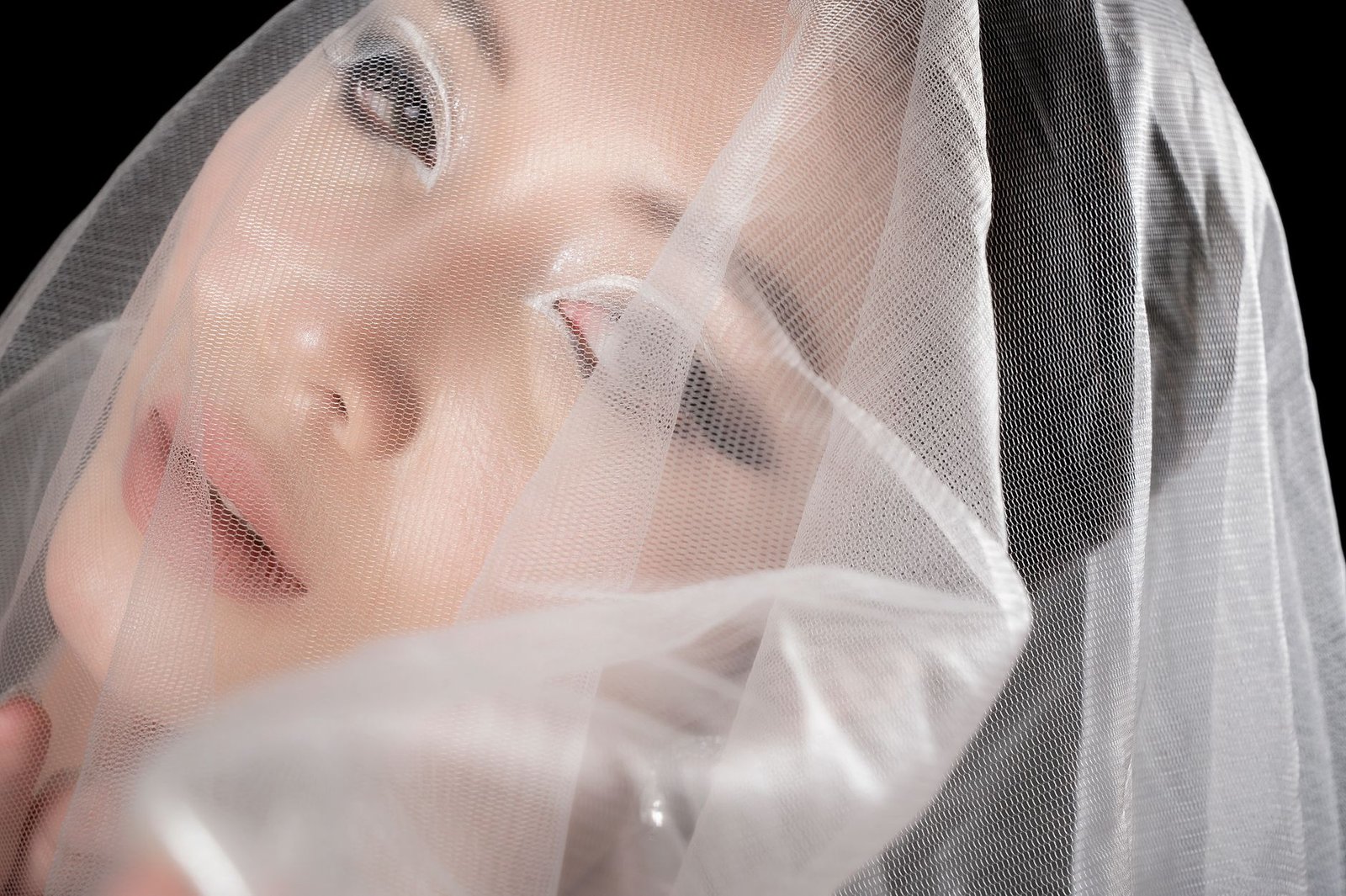 Close-up portrait of a person under a soft white veil creating an artistic and ethereal effect.