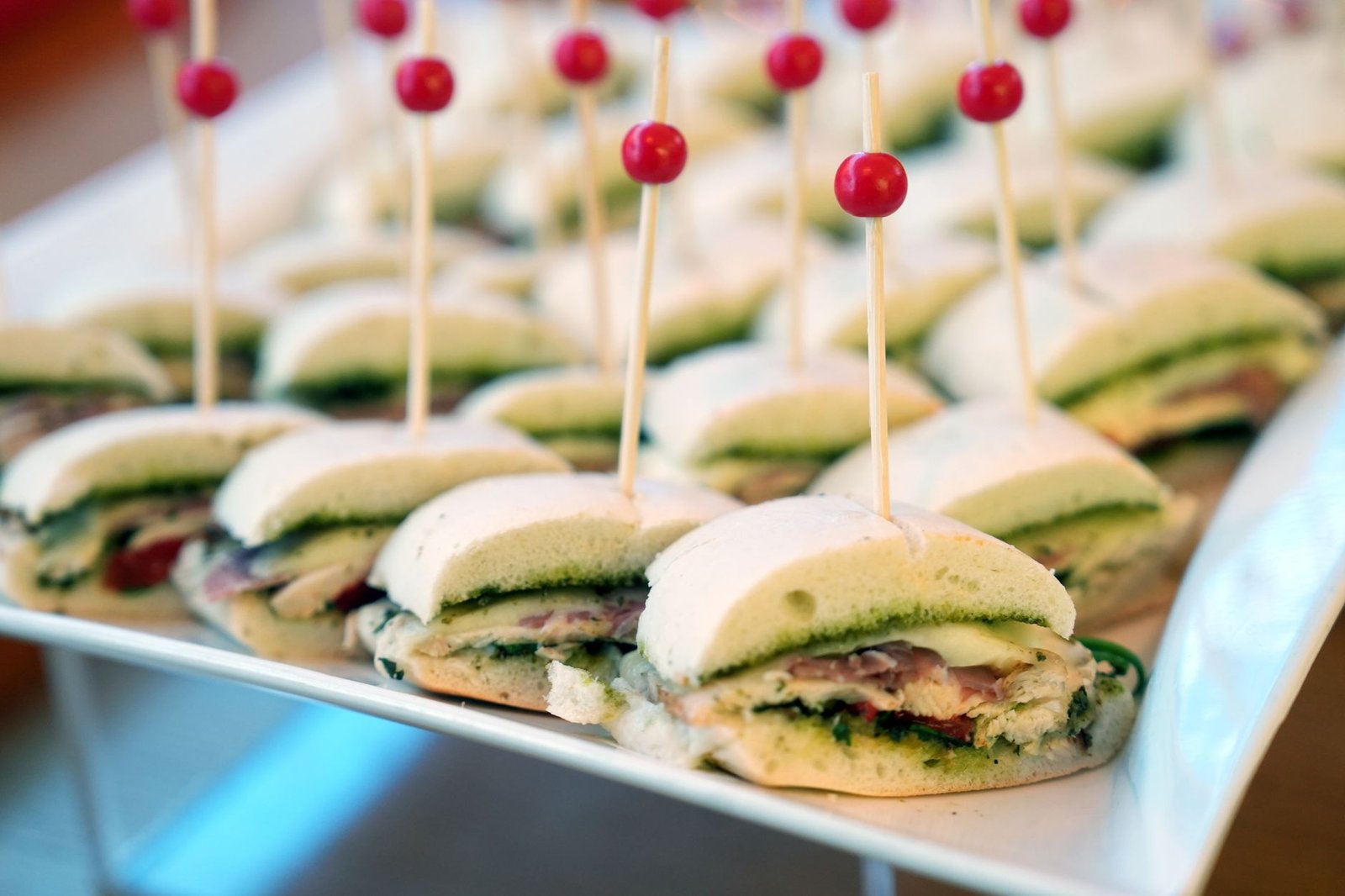 A plate of delicious mini sandwich appetizers garnished with red picks, perfect for a party or event.