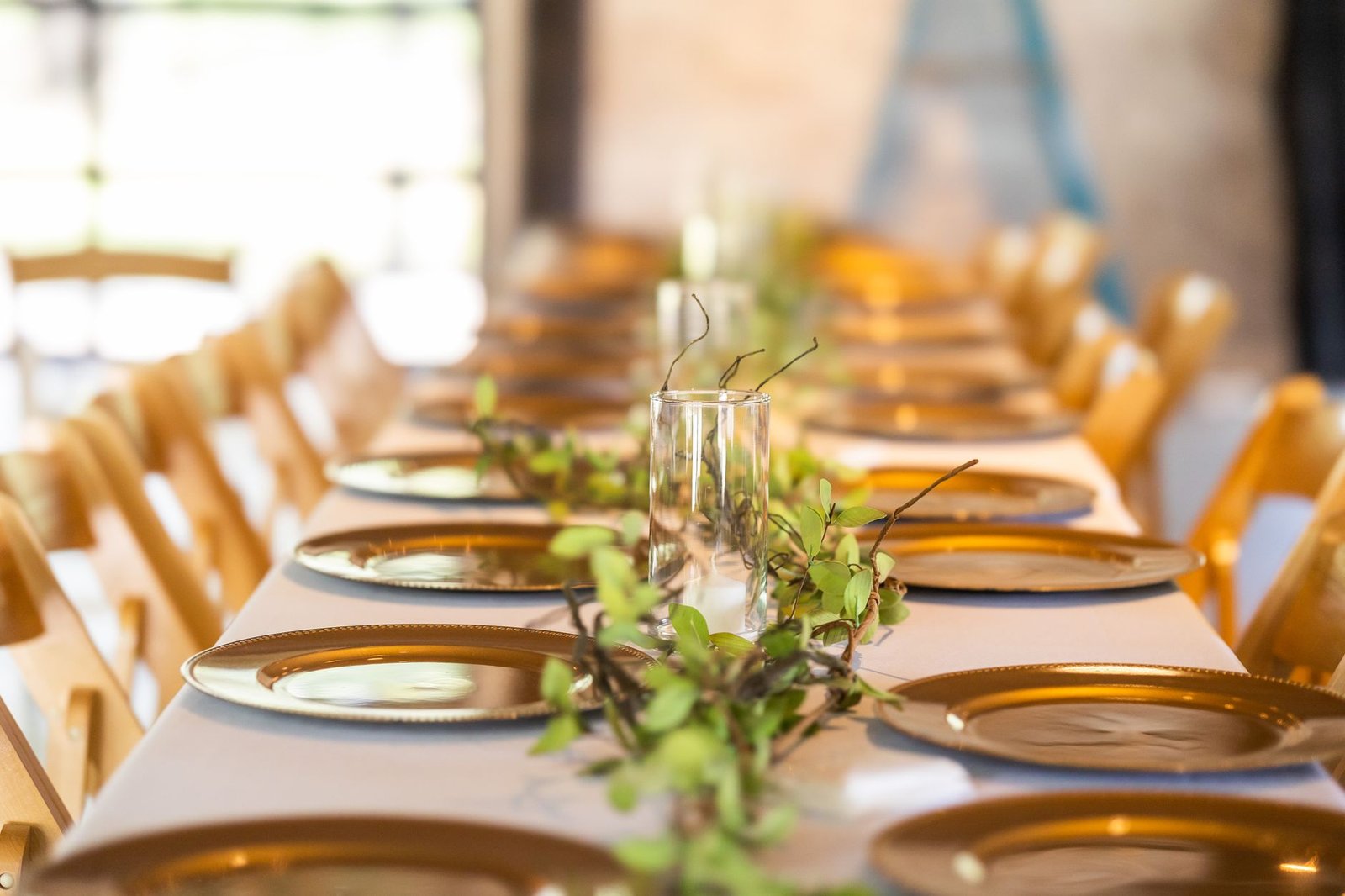 Elegant dining table setup with gold plates and lush greenery centerpiece, perfect for weddings or events.