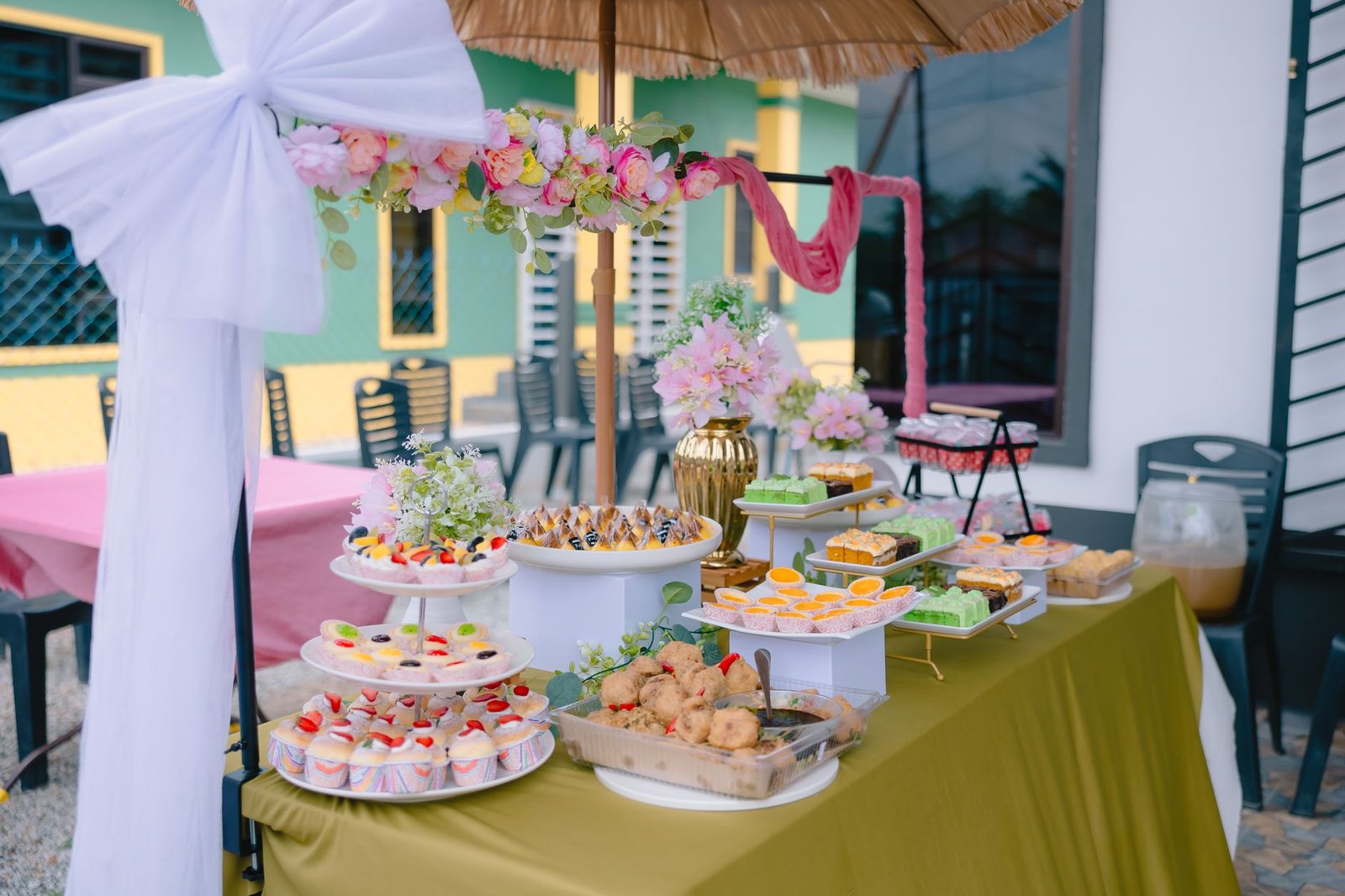 A beautifully arranged outdoor buffet table featuring a variety of decorated desserts under a floral canopy.