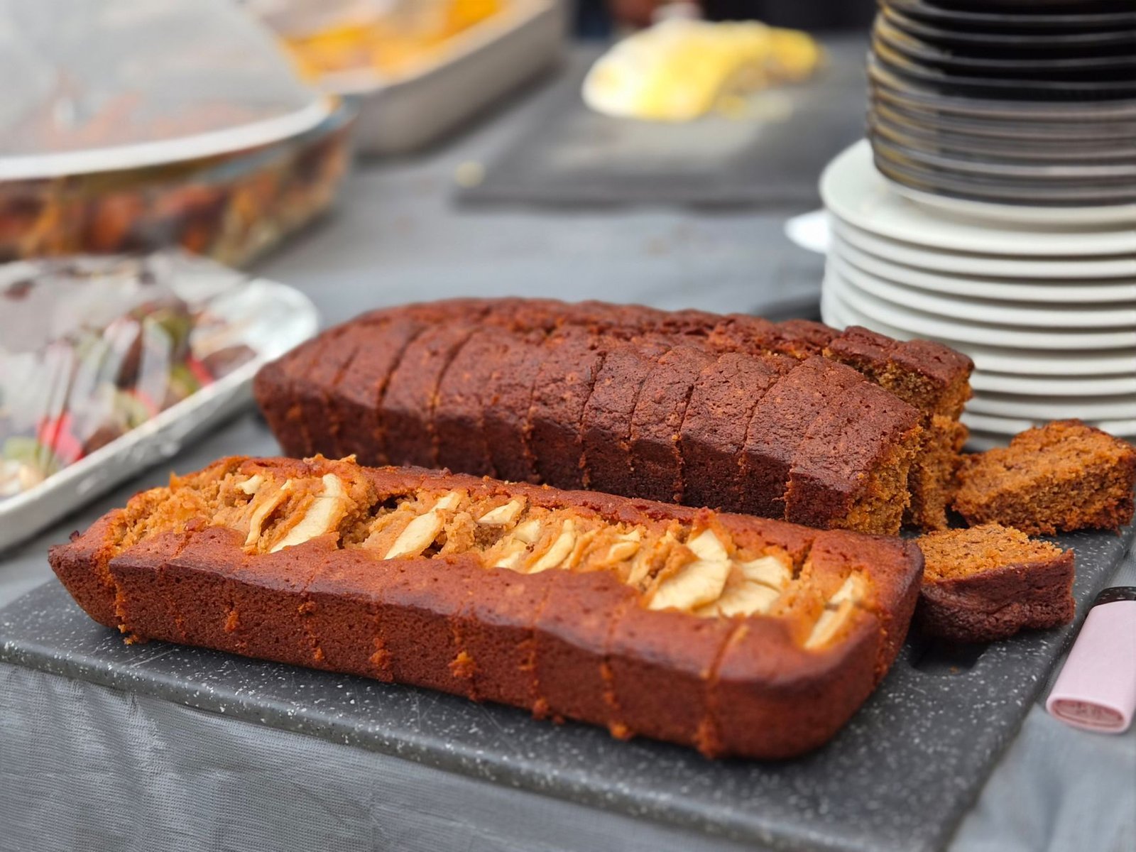 Close-up of sliced apple and gingerbread loaves served on a tabletop at an outdoor event.