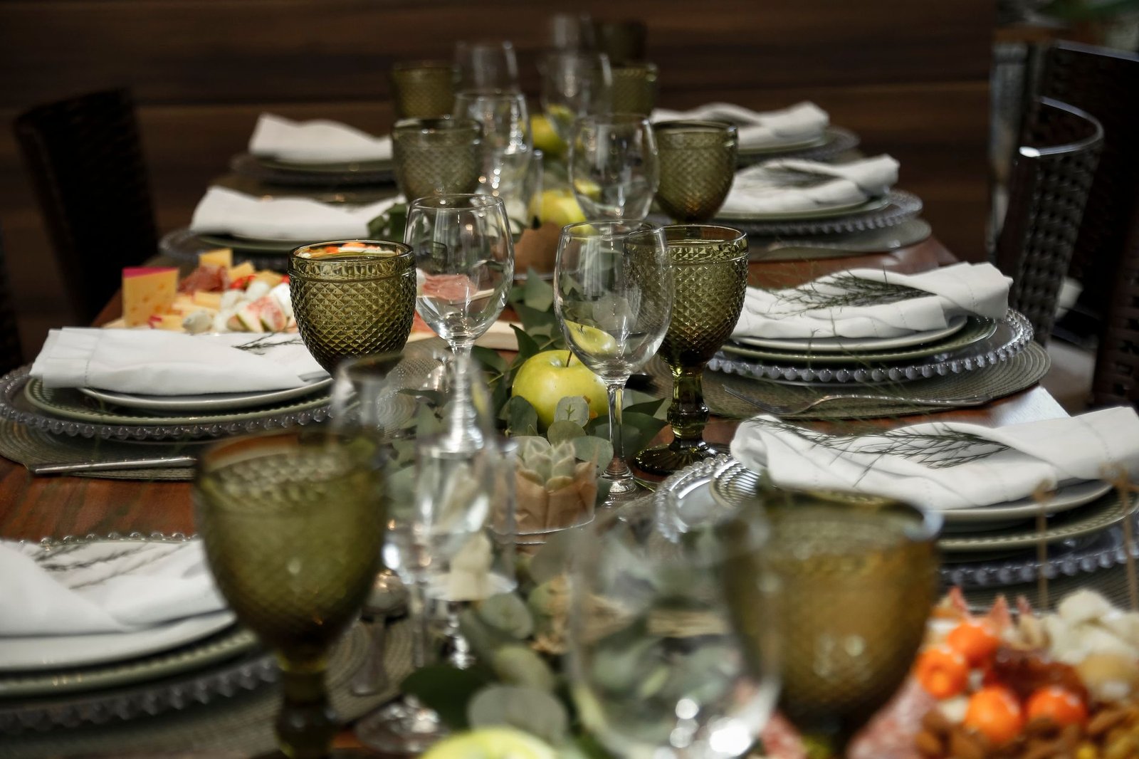 A beautifully arranged dinner table with green goblets and fresh apples.