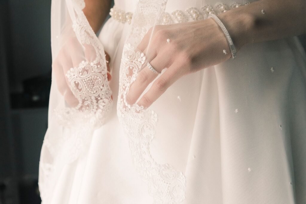 Kedekatan tangan pengantin perempuan yang menyesuaikan sluff bridal renda, menampilkan keanggunan dan detail.