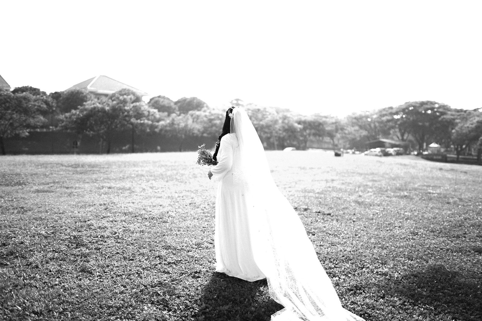 Pengantin wanita anggun dalam hitam putih berdiri di lapangan terbuka, menciptakan momen pernikahan yang abadi.