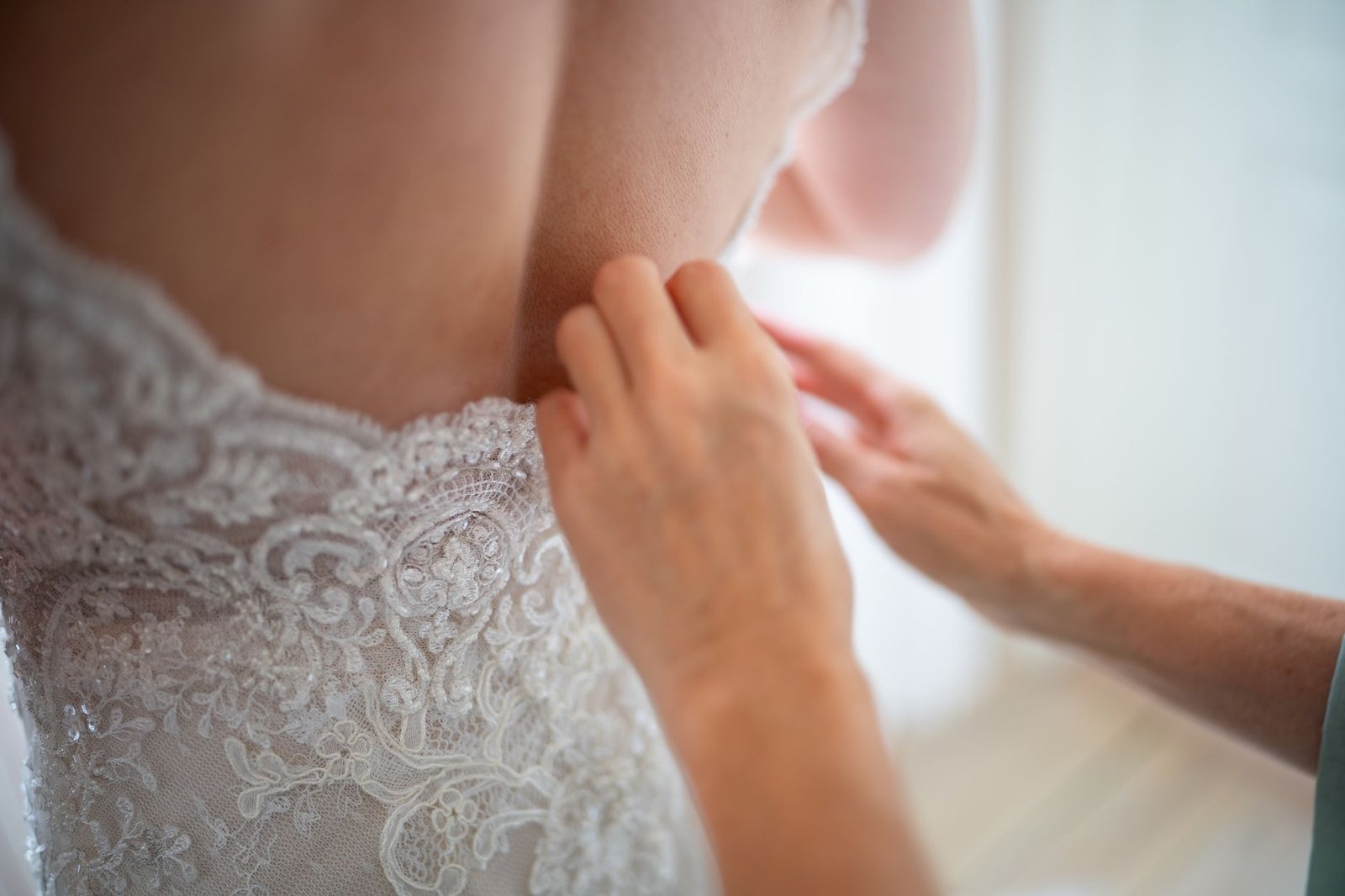 Close-up of a bride's wedding dress being adjusted, showcasing intricate lace details.