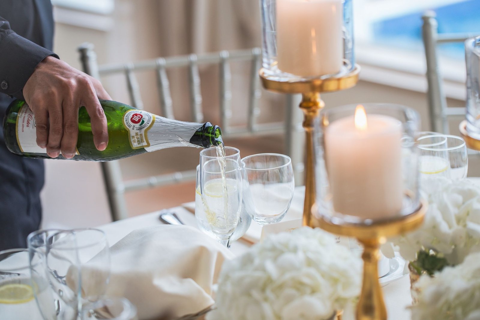 A hand pours champagne into glasses at an elegant, candle-lit table setting.