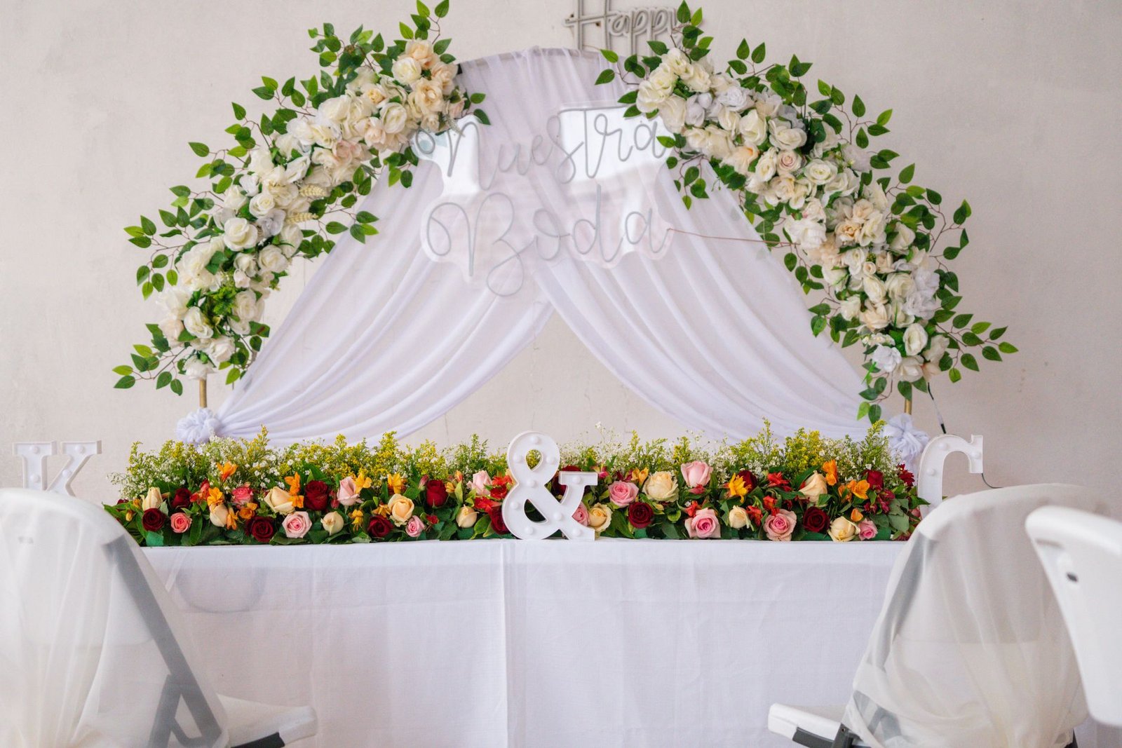 Beautifully decorated wedding table adorned with roses, greenery, and draped white fabric.