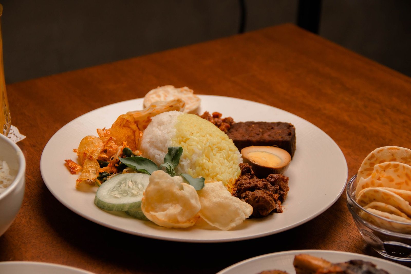 Plate of Nasi Padang with rice, egg, vegetables, and meat on a wooden table.