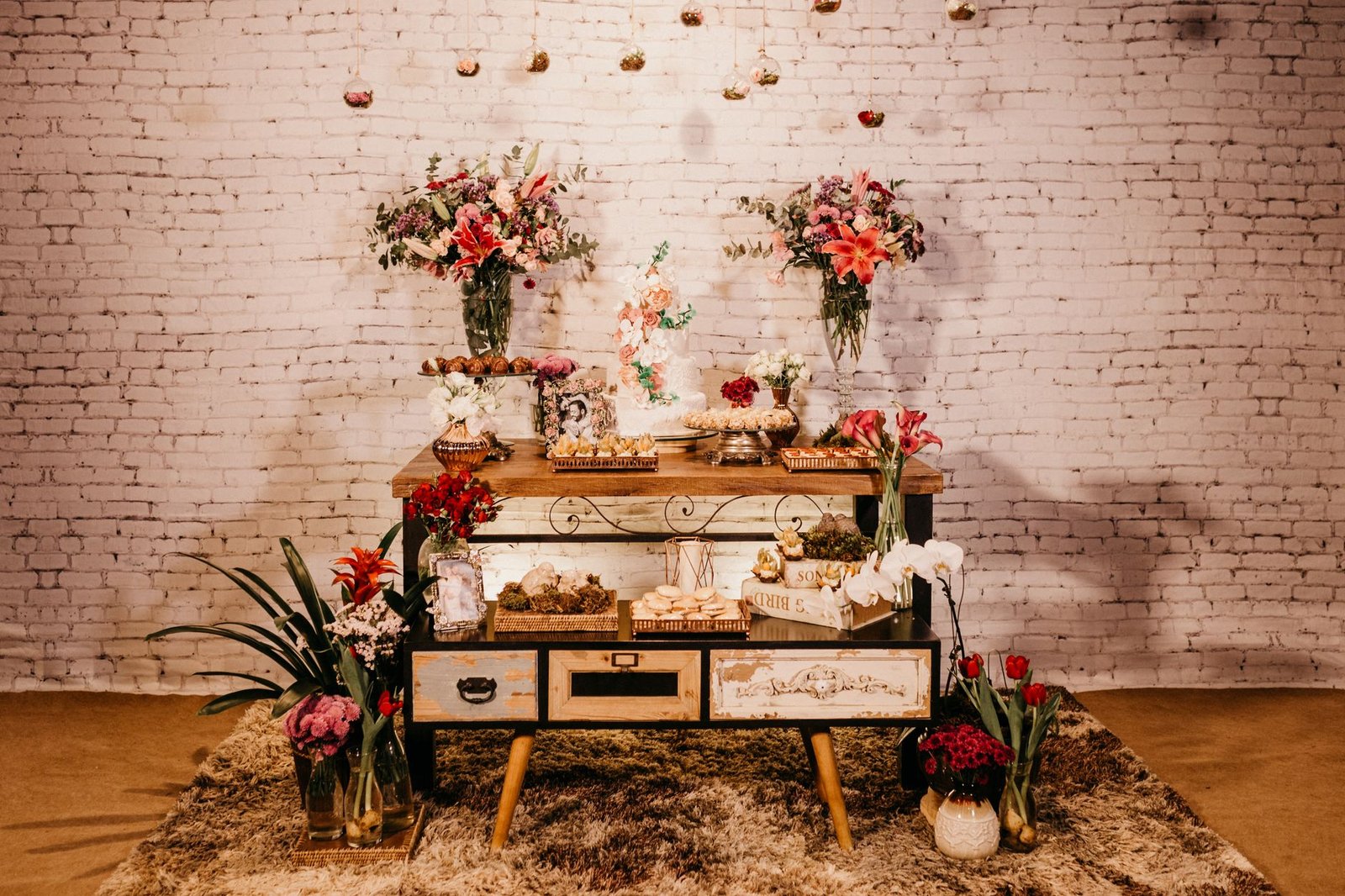 Assorted delicious sweets served on creative wooden cabinet on fluffy carpet decorated with bright fragrant flowers bouquets in light studio