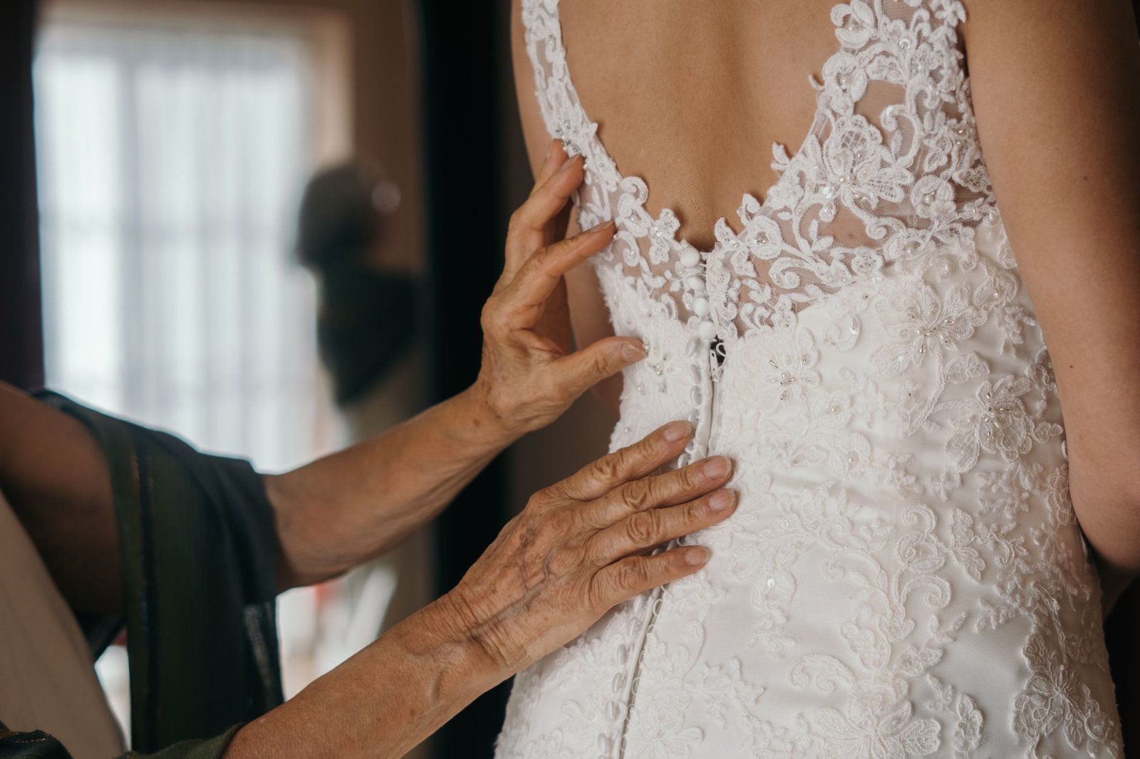 Detailed view of a bride's lace wedding dress being adjusted indoors by a seamstress.
